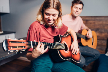Obraz premium lovely couple, young people playing guitar together at home sitting on bed. caucasian girl and boy wearing casual home clothes