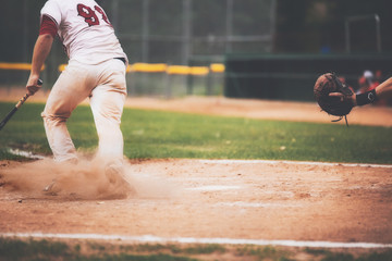 The bottom half of a male baseball player with a cloud of red dust around his feet as he starts running