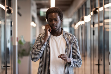 Concentrated african entrepreneur walking in office hallway talking on phone