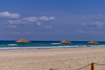 Thatched umbrellas on a sandy beach. Sea. The waves. The clouds. Coast.