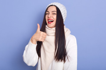 Portrait of emotional magnetic cute female laughing, having positive emotions, raising thumb, making gesture, being in good mood, opening mouth widely, having red lips. People and mood concept.