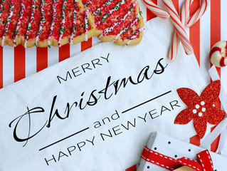 Christmas cookies and decor surround a white napkin on a cheerful red and white striped background....