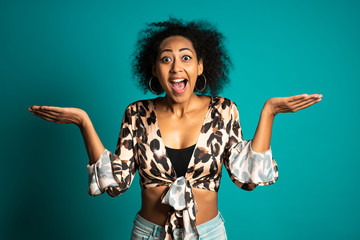 Pretty african american woman with afro hair in leopard wear smiling, pleasantly surprised to camera over blue wall background. 