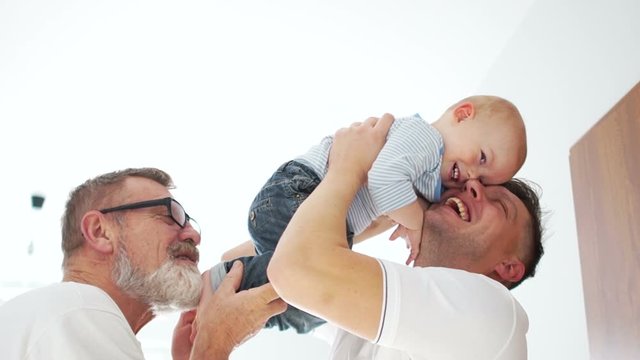 Happy men of the same family. Three men, grandfather, father and grandson. Father's day. Men hug baby indore in white room