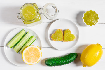 Homemade cucumber jam with lemon and heart-shaped toast on a white wooden background.