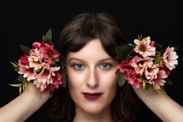 Naklejka premium Close-up of a brown-haired girl and blue eyes with two bouquets of flowers in hands