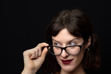 Close-up of a woman with brown hair and blue eyes while resting her glasses on her nose, myopia concept