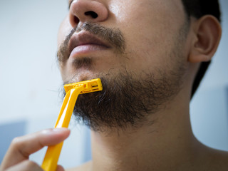closeup man use yellow shaver shaving messy beard and mustache on his face in bathroom - 306733063