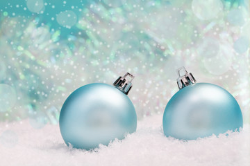 Merry Christmas or Happy new year greeting card with turquoise christmas balls on snow on snowy and bokeh backdrop.