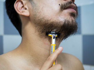 closeup man use yellow shaver shaving messy beard and mustache on his face in bathroom - 306733282
