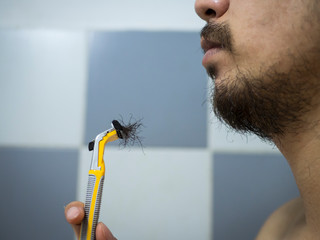 closeup man use yellow shaver shaving messy beard and mustache on his face in bathroom - 306733436