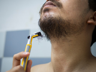 closeup man use yellow shaver shaving messy beard and mustache on his face in bathroom - 306733456