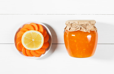 Delicious homemade carrot jam with lemon in a glass jar on a white wooden background.