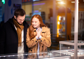 newly married couple, caucasian man and woman during shopping in mall, choose expensive jewelry for female, wearing coat and hugging man