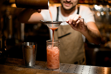 Fototapeta na wymiar Bartender flows drink through sieve to glass