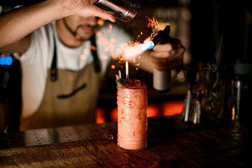 Fototapeta na wymiar Bartender fires up alcohol cocktail with burner