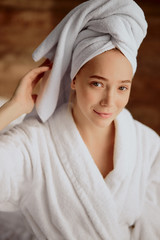 Obraz premium Beautiful young woman after bath with towel wrapped on head, looking straight at camera with charming smile, raising hand up, portrait, natural beauty concept