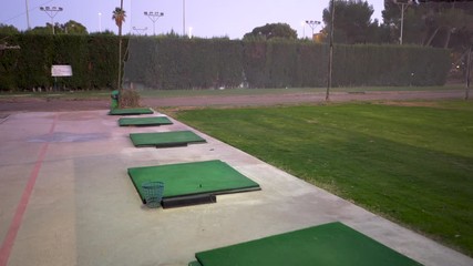 Traveling from a practice area in a golf club, the field is green and with hiber, the shooting mats put in line towards the shooting zone - Powered by Adobe