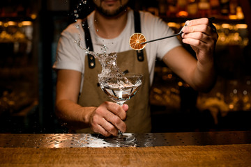 Close shot of bartender decorating splashing alcohol with orange