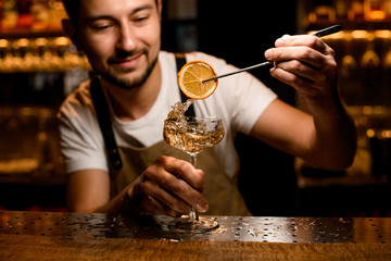 Smiling bartender puts orange slice in alcohol drink