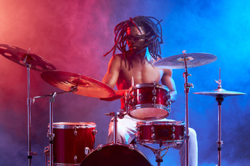 Obraz na płótnie Canvas vigorous male with naked skin playing on drums isolated over neon smoky background, wearing eyeglasses