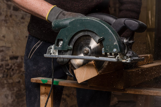 Building constractor worker with gloves using hand held worm driver circular saw.