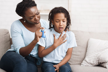 Black mother holding asthma inhaler for daughter