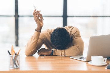 Exhausted african american businessman holding mobile phone