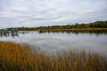 A boat is speeding down the waterway. The calm water is surrounded by grass in the waterway.