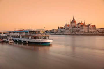 Hungarian parliament and boat. Amazind morning lights with blurred water. Boat cruise, long exposure, danube river