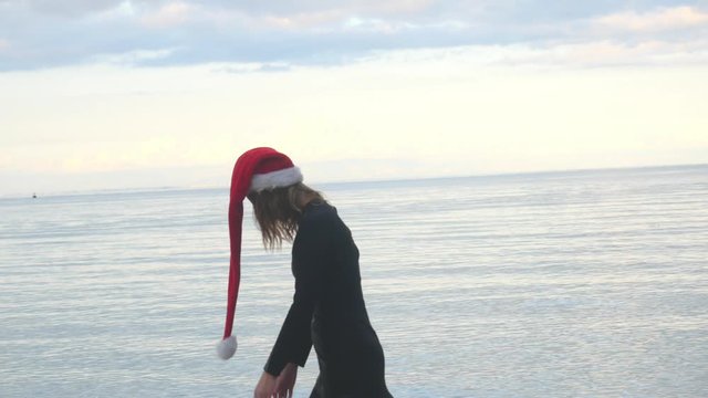 Woman in Santa hat sadly walking by the sea