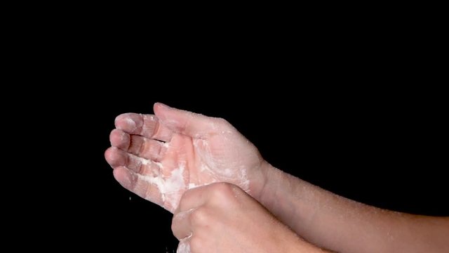 A person rubbing his hands and evenly distributing the chalk powder, isolated on black background. Slow motion.