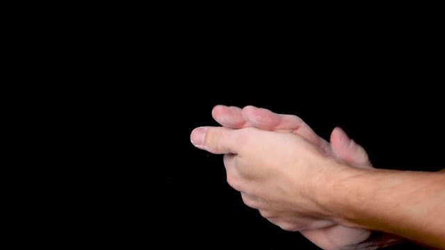 A person rubbing and dusting his hands with chalk powder, isolated on black background. Slow motion.