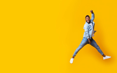 Fototapeta na wymiar Portrait of jumping black guy on yellow studio background