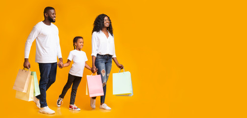 Happy black family of three walking with colourful shopping bags