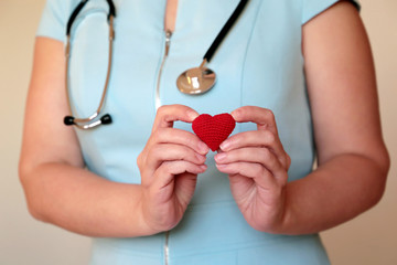 Cardiology and health care, woman doctor holding red knitted heart in hands. Concept of cardiologist, blood donation, treatment of heart disease in the clinic