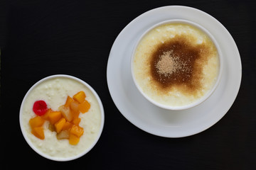 Two bowls of porridge in different flavors stand side by side against a black background and contain fruit or cinnamon with sugar