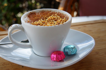 a cup of traditional Turkish coffee like hot drink called sahlep, served by cinnamon powder on it and with two pieces of chocolate placed on its plate