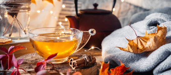 Cozy autumn or winter at home. A cup of tea, autumn casts a book a garland on a wooden table near a bed with warm plaids. Lifestyle autumn hygge lagom?concept of a holiday and autumn weekend.Banner