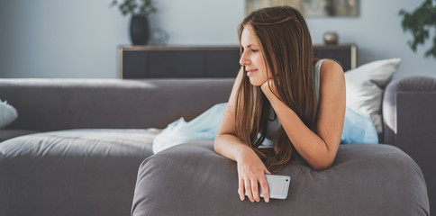Obraz premium portrait of young teenager brunette girl with long hair lying on sofa at home have fun using smartphone