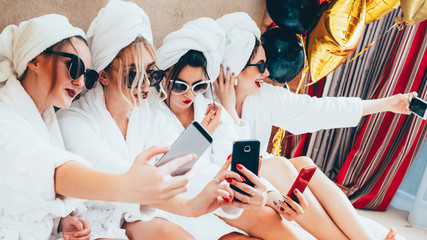 Social media addiction. Modern women leisure. Ladies in bathrobes taking selfies at home party.