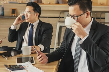 Two  businessman during break time in office drinking coffee and using phone.