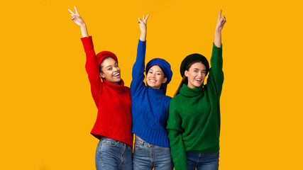 Obraz premium Three Girls Gesturing Victory Sign Raising Hands Standing, Yellow Background