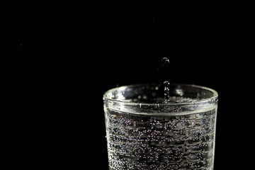 Water falling into a glass forming splashes on a black background under studio lighting