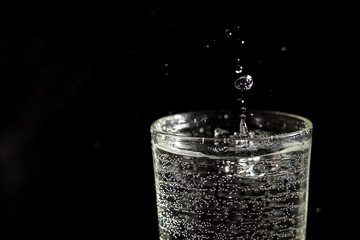 Water falling into a glass forming splashes on a black background under studio lighting