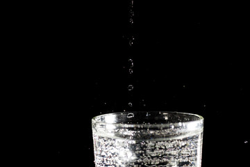 Water falling into a glass forming splashes on a black background under studio lighting