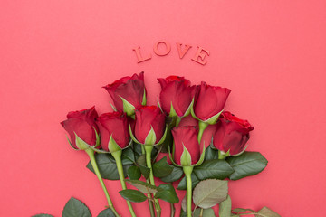 Fototapeta premium Red roses and LOVE letters inscription, over pink background flat lay. Valentine's Day, Birthday abstract background with copy space.