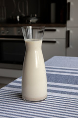 Fresh vegan homemade oat milk in glass carafe standing on the kitchen table. Non dairy diet.