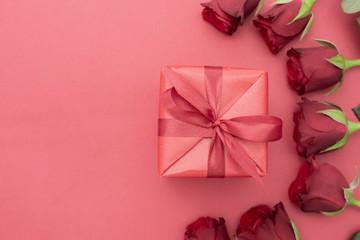 Valentine's Day, red roses and gift box with ribbon, over red background flat lay, birthday abstract background with copy space.