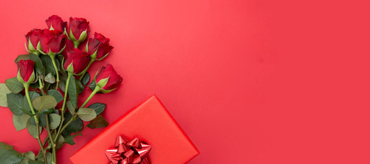 Red roses and gift box with ribbon, over red background flat lay. Valentine's Day, Birthday...